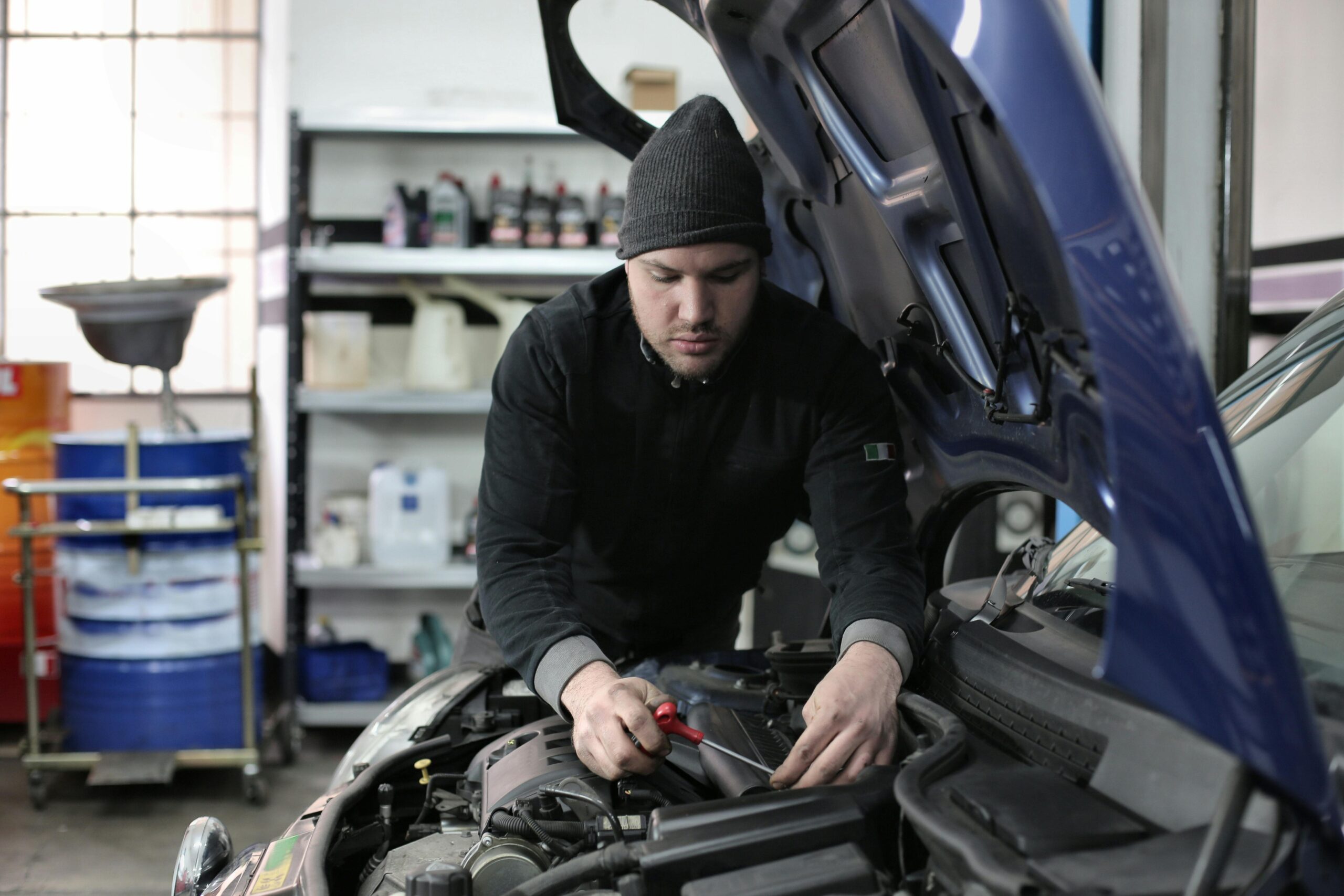 Man working under car hood in a garage, focused on engine repair