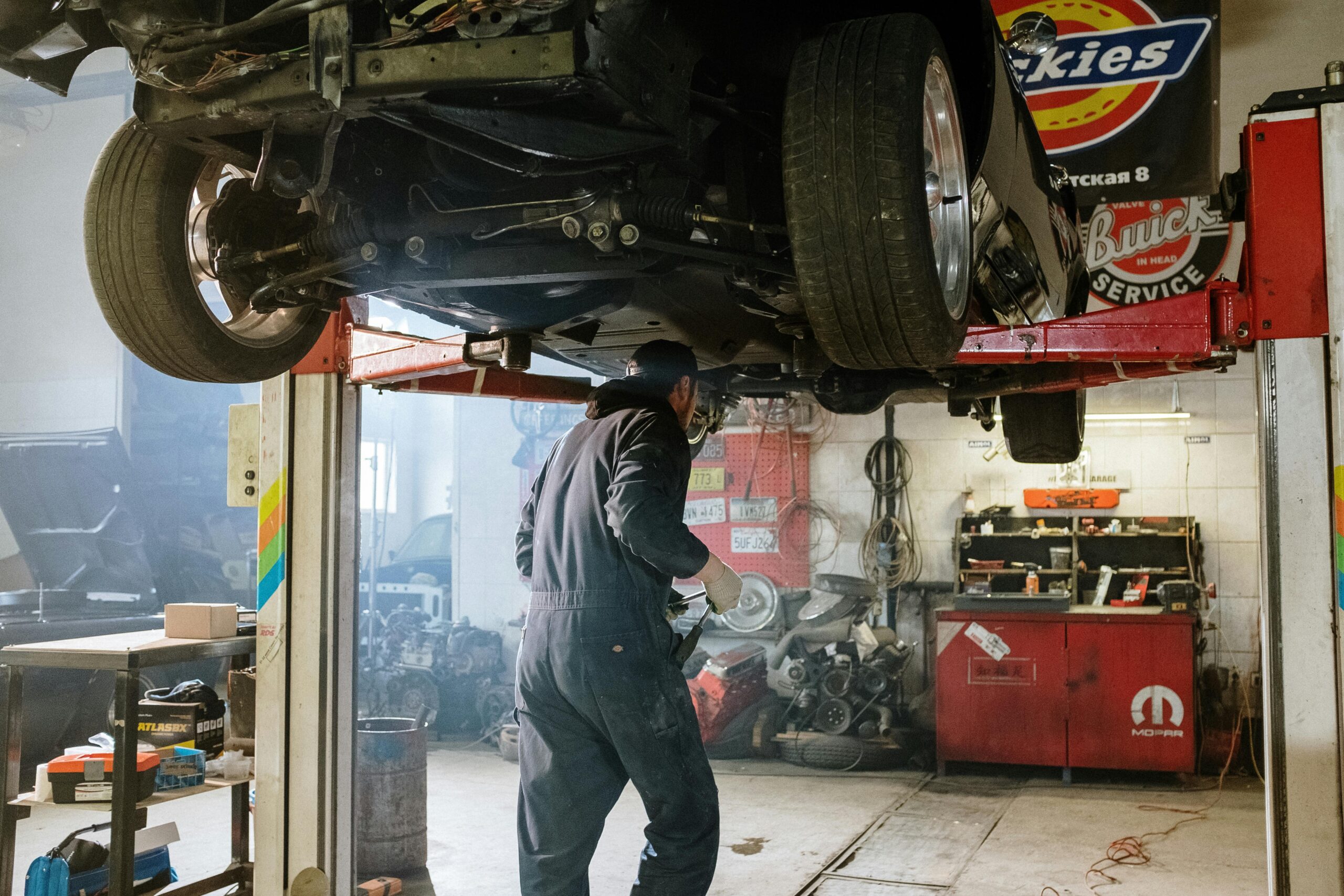 Mechanic repairing a vehicle in a busy workshop with various automotive tools.