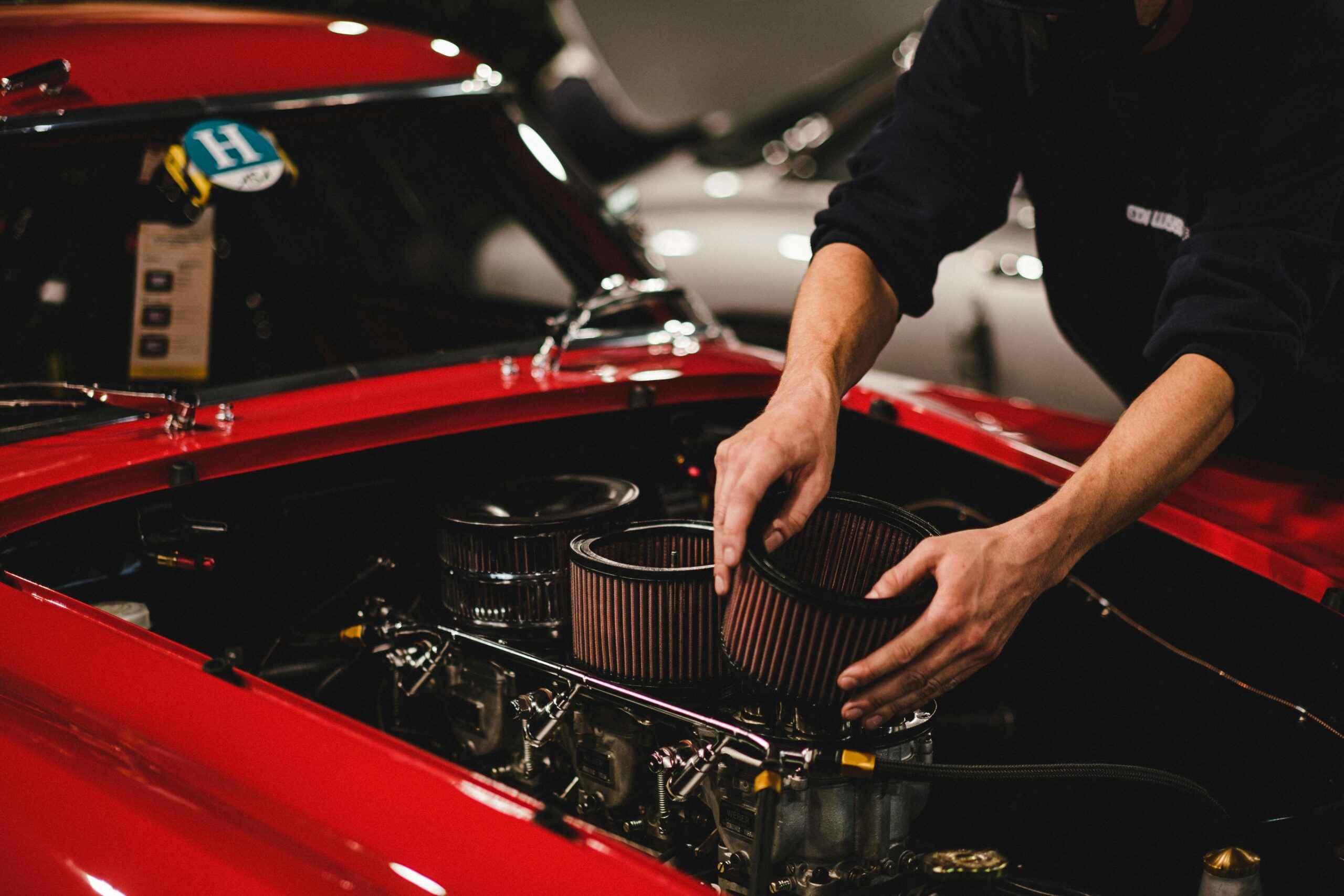 Close-up of a mechanic working on a car engine in a garage setting, focusing on air filter adjustment.