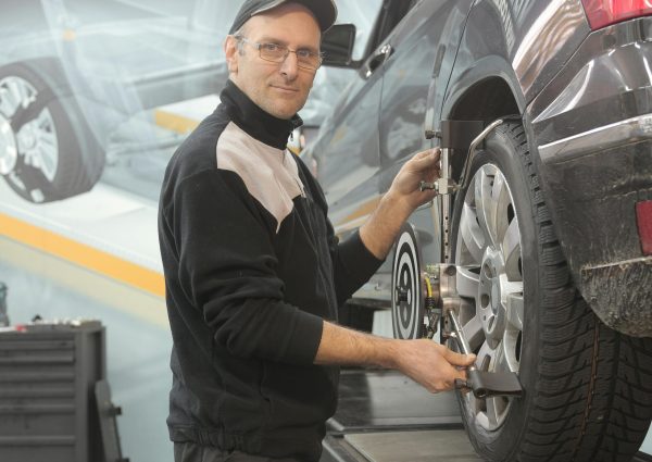 Mechanic performing wheel alignment on a car in a professional garage setting.